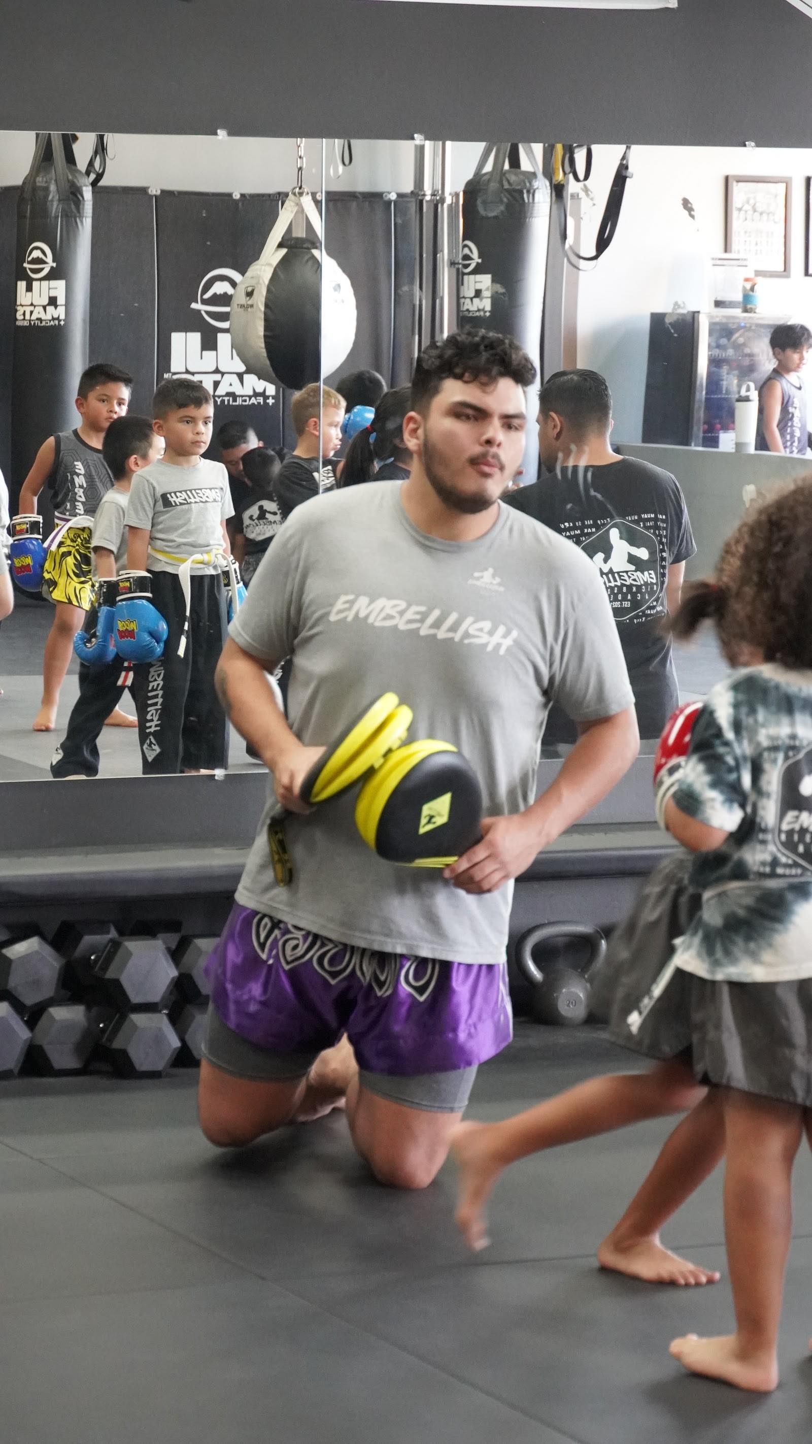 Embellish Kickboxing Academy coach kneeling to hold pads for a young student in Elk Grove.